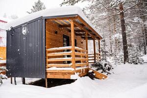 modulair huis gemaakt van donker metaal en licht hout in winter Woud. een huis dat duurt in account alles u nodig hebben voor een comfortabel leven buiten de stad. foto