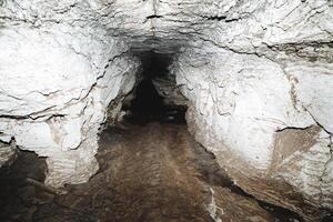 speleologie wandeltocht naar de grot, lantaarn verlicht de ondergronds afgrond karst vorming, limoen grot, passage vuil bodem klei. foto
