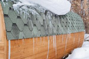 ijspegels hangen Aan de dak van de huis. voorjaar smelt sneeuw, ijs smelt van de dak van de huis. dakbedekking dak tegels Aan de dak. foto