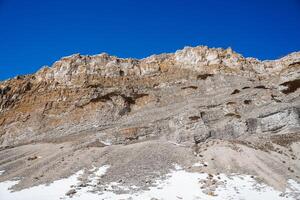 de hoog kliffen zijn grijs. de top van een steen berg tegen de lucht, sneeuw viel Bij de voet van de bergen. visie van hieronder van de hoog bergen. foto