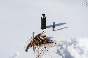 uitrusting voor wandelen leugens Aan de sneeuw, een thermosfles met heet thee, een mes met een geel handvat, brandhout, camping in de winter in de Woud. foto