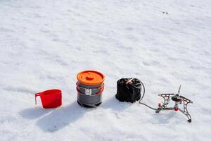 een reeks van kamp gebruiksvoorwerpen, camping apparatuur, Koken in camping conditie, een pan staat Aan de sneeuw, een gas- brander met een slang voor een propaan cilinder foto