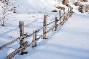 houten hek in winter onder de sneeuw, corral voor vee, hekwerk Aan de boerderij voor dieren. winter landschap. een barrière gemaakt van logboeken van oud bomen. foto