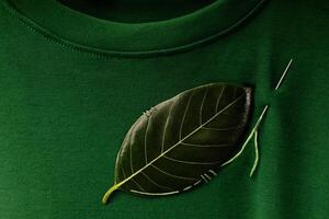 esg en duurzaamheid levensstijl. milieu zorg concept. dichtbij omhoog van een groen blad geborduurd met een naaien naald- Aan t-shirt. milieuvriendelijk, biologisch kleding foto