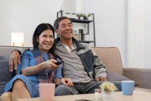 Aziatisch senior paar genieten van in hun favoriete TV. gelukkig pensioen paar aan het kijken televisie samen in leven kamer foto