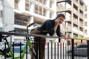 zakenman en fiets in stad naar werk met eco vriendelijk vervoer. fiets en gelukkig zakenman professioneel praten, sprekend en telefoon discussie terwijl Aan in stedelijk straat foto