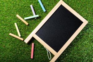 bovenaanzicht van mini schoolbord en kleuren op kunststof gras achtergrond. concept terug naar school foto
