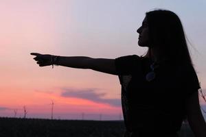 mooie jonge brunette meisje poseren een weg in het midden van het veld bij zonsondergang, silhouette foto