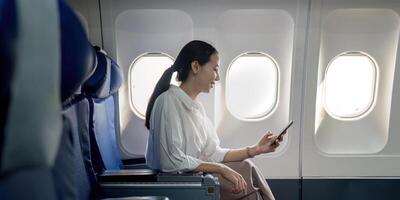 geslaagd jong Aziatisch bedrijf vrouw zit in vliegtuig cabine vlak en werken van overal. vliegend Bij eerste klasse foto