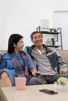 Aziatisch senior paar genieten van in hun favoriete TV. gelukkig pensioen paar aan het kijken televisie samen in leven kamer foto