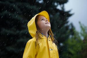 ai gegenereerd een weinig meisje in een geel regenjas verheugt zich terwijl staand in de voorjaar regen foto