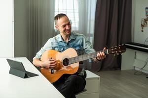 Kaukasisch Mens van een afstand geeft les gitaar spelen Aan de laptop. online muziek- opleiding foto