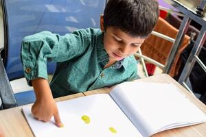 slim Indisch weinig jongen uitvoeren duim schilderij met verschillend kleurrijk water kleur uitrusting gedurende de zomer vakanties, schattig Indisch kind aan het doen kleurrijk duim schilderij tekening Aan houten tafel foto