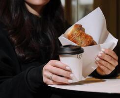 meisje aan het eten croissant met pistache poeder en drinken koffie Aan terras foto