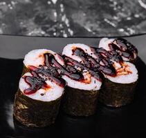 sushi rollen maki met paling en unagi saus Aan een zwart bord foto