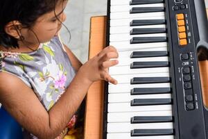 Aziatisch schattig meisje spelen de synthesizer of piano. schattig weinig kind aan het leren hoe naar Speel piano. kind handen Aan de toetsenbord binnen. foto