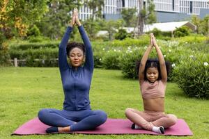 Afrikaanse Amerikaans vrouw en haar dochter in yoga pak zijn ontspannend beoefenen meditatie oefening in de park naar bereiken geluk van binnenste vrede wijsheid voor gezond geest en ziel foto