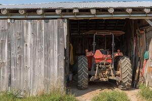 trekker geparkeerd in een schuur met boerderij gereedschap en uitrusting Aan een zonnig laat middag foto