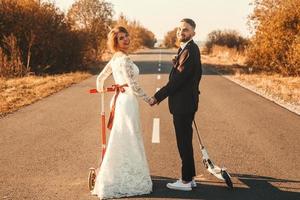 lachend bruidspaar rijden op scooters langs de weg buiten de stad bij zonsondergang. foto