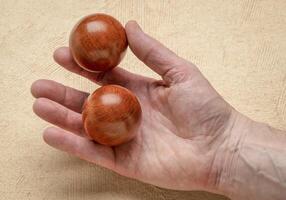 mannetje hand- Holding een paar- van houten Chinese geneeskunde ballen tegen getextureerde papier foto