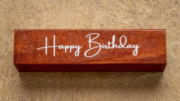 gelukkig verjaardag tekst Aan houten blok tegen handgemaakt schors papier in aarde tonen, groet concept foto
