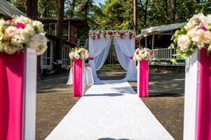 mooi bruiloft ceremonie buitenshuis. bruiloft boog gemaakt van kleding en wit en roze bloemen Aan een restaurant achtergrond. foto