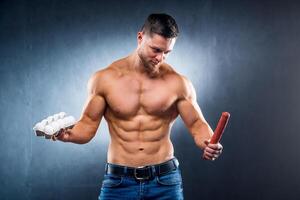 bodybuilder sportman Holding eieren en worst . kiezen tussen gezond en schadelijk voedsel. naakt torso. grijs achtergrond. detailopname foto
