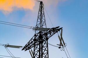 hoog Spanning macht toren en mooi natuur landschap Bij zonsondergang. elektriciteit pyloon Aan blauw lucht achtergrond. foto