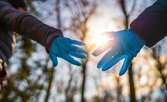 twee handen in rubber medisch handschoenen tegen zonsondergang . romantisch relaties tussen mensen. bescherming, isolatie en afstand gedurende de covid-19 coronavirus pandemie. foto
