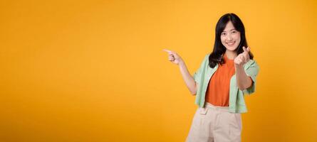 jong Jaren 30 Aziatisch vrouw vervelend een groen overhemd Aan een oranje achtergrond points vingers naar vrij kopiëren ruimte terwijl tonen een mini hart hand- teken. onderzoeken de wereld van korting boodschappen doen Promotie concept. foto
