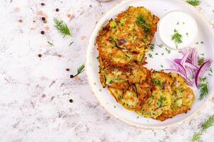 courgette beignets met rood uien, knoflook en kruiden. vegetarisch courgette pannekoeken en verzuren room Aan wit tafel. top visie foto