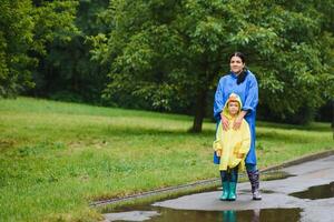 mam en zoon in regenjassen hebben pret samen in de regen. concept van familie vakantie en gelukkig jeugd. foto