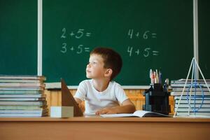 onderwijs en aan het leren. weinig schooljongen in klas. schooljongen aan het doen huiswerk in klas Bij school. elementair school- kind zittend Bij bureau. onderwijs. kind Bij school. foto