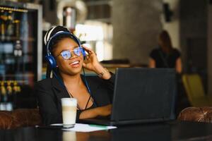 jong Afrikaanse Amerikaans meisje zittend Bij cafe tafel met laptop en op zoek Bij scherm. donker huid freelancer concept. foto