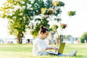 weinig meisje zittend in de park en werken met laptop. opleiding, levensstijl, technologie concept foto