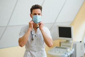 mannetje dokter in masker met echografie uitrusting in de kliniek kantoor foto