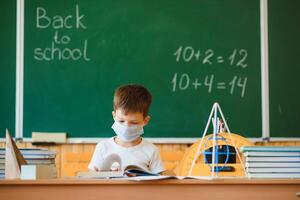 schooljongen in de klas in een beschermend masker. de concept van scholing gedurende de epidemie foto