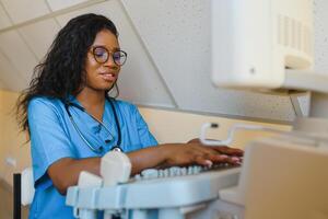 glimlachen Afrikaanse vrouw dokter met echografie scanner in hand, werken Aan modern echografie scannen machine in licht kamer in kliniek. portret van 4d echografie scannen machine operator foto