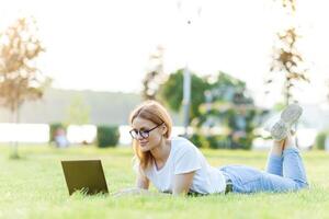 mooi vrouw werken met laptop in de park Aan de gras. de concept van afgelegen werk foto