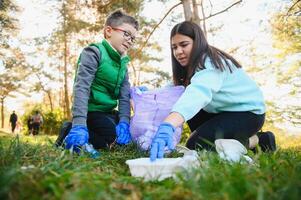 mam geeft les haar zoon naar schoon omhoog uitschot in natuur. een vrouw verwijdert plastic flessen in een tas. de onderwerp van milieu verontreiniging door afval. foto