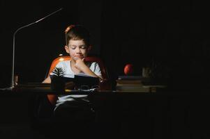 schooljongen aan het doen huiswerk Bij de tafel in zijn kamer. foto