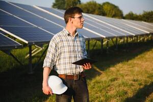 de portret van een jong ingenieur cheques met tablet operatie met zon, netheid Aan veld- van fotovoltaïsche zonne- panelen. concept hernieuwbaar energie, technologie, elektriciteit, onderhoud, groen stroom. foto