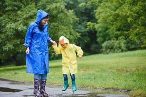 mam en zoon in regenjassen hebben pret samen in de regen. concept van familie vakantie en gelukkig jeugd. foto