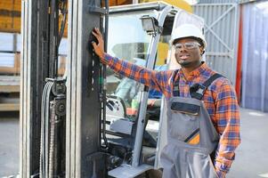 portret van een gelukkig Afrikaanse Amerikaans mannetje arbeider het rijden heftruck Bij werkplaats foto