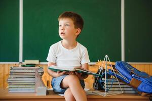 onderwijs en aan het leren. weinig schooljongen in klas. schooljongen aan het doen huiswerk in klas Bij school. elementair school- kind zittend Bij bureau. onderwijs. kind Bij school. foto