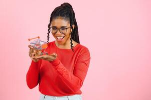 Afrikaanse Amerikaans meisje met boodschappen doen kar Aan roze achtergrond. de concept van winstgevend verkoop of aankopen foto