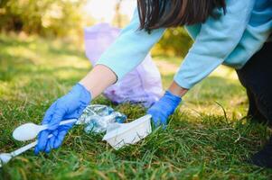 vrouwen handen in rood rubber handschoenen. vrouw verzamelt uitschot in de tas. vrijwilliger opruimen vuilnis in de zomer park. mooi hoor progressief vrouw maken een inspanning naar helpen de milieu foto