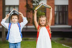 gelukkig kinderen - jongen en meisje met boeken en rugzakken Aan de eerste school- dag. opgewonden naar worden terug naar school- na vakantie. vol lengte buitenshuis portret. foto