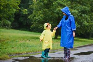 mam en zoon in regenjassen hebben pret samen in de regen. concept van familie vakantie en gelukkig jeugd. foto