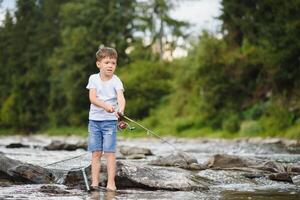 schattig jongen in wit t overhemd visvangst in de rivier- en heeft plezier, glimlacht. vakantie met kinderen, vakantie, actief weekends concept foto